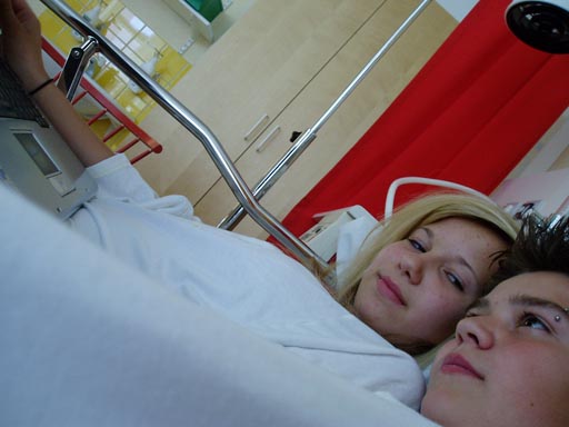 Ossi och Klara ligger bredvid varandra iklädda sjukhuskläder i en sjukhussäng. Klara tittar på Ossi.